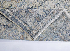 A vintage Persian Kerman rug with a blue and beige floral medallion pattern folded to show detail.