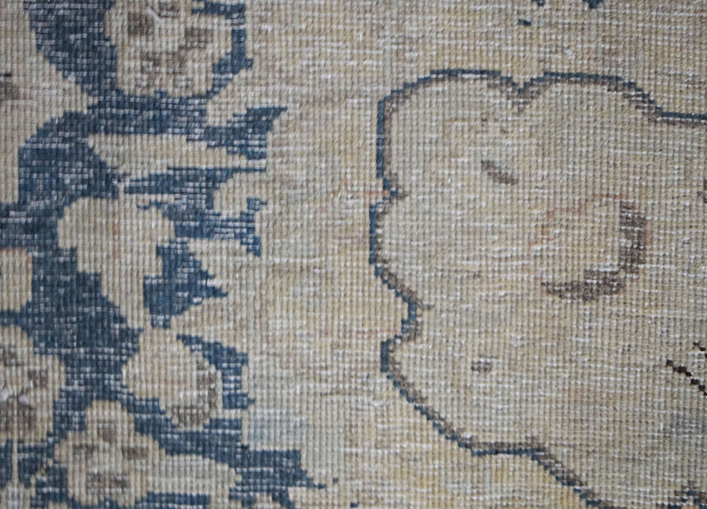 A close-up of a vintage Persian Kerman rug featuring intricate blue floral patterns on a tan base.