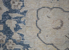 A close-up of a vintage Persian Kerman rug featuring intricate blue floral patterns on a tan base.
