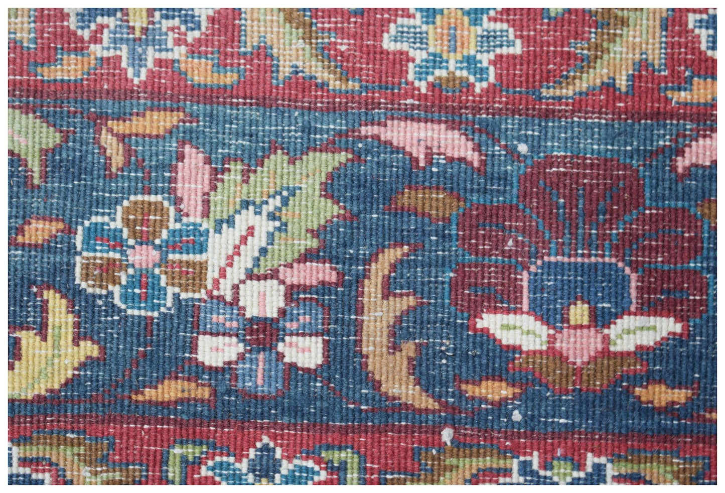 A close-up of a vintage Persian Kerman rug featuring intricate floral patterns in blue and red.