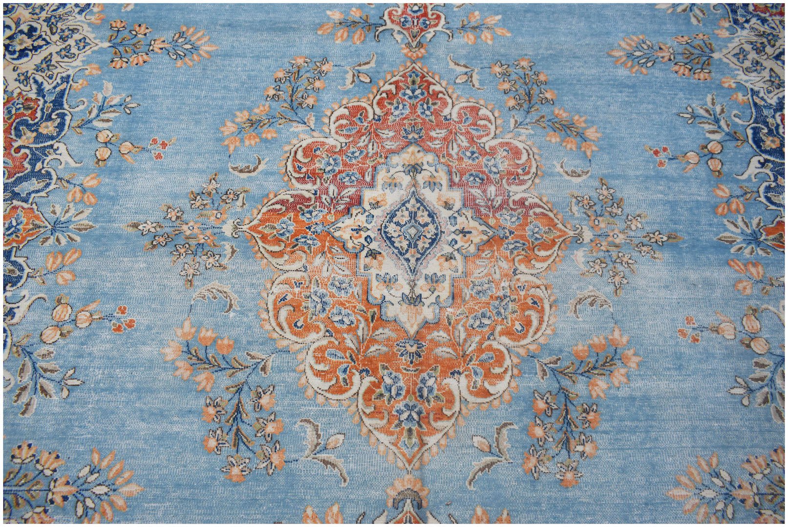 A vintage Persian Kerman rug featuring a central floral medallion on a light blue field.