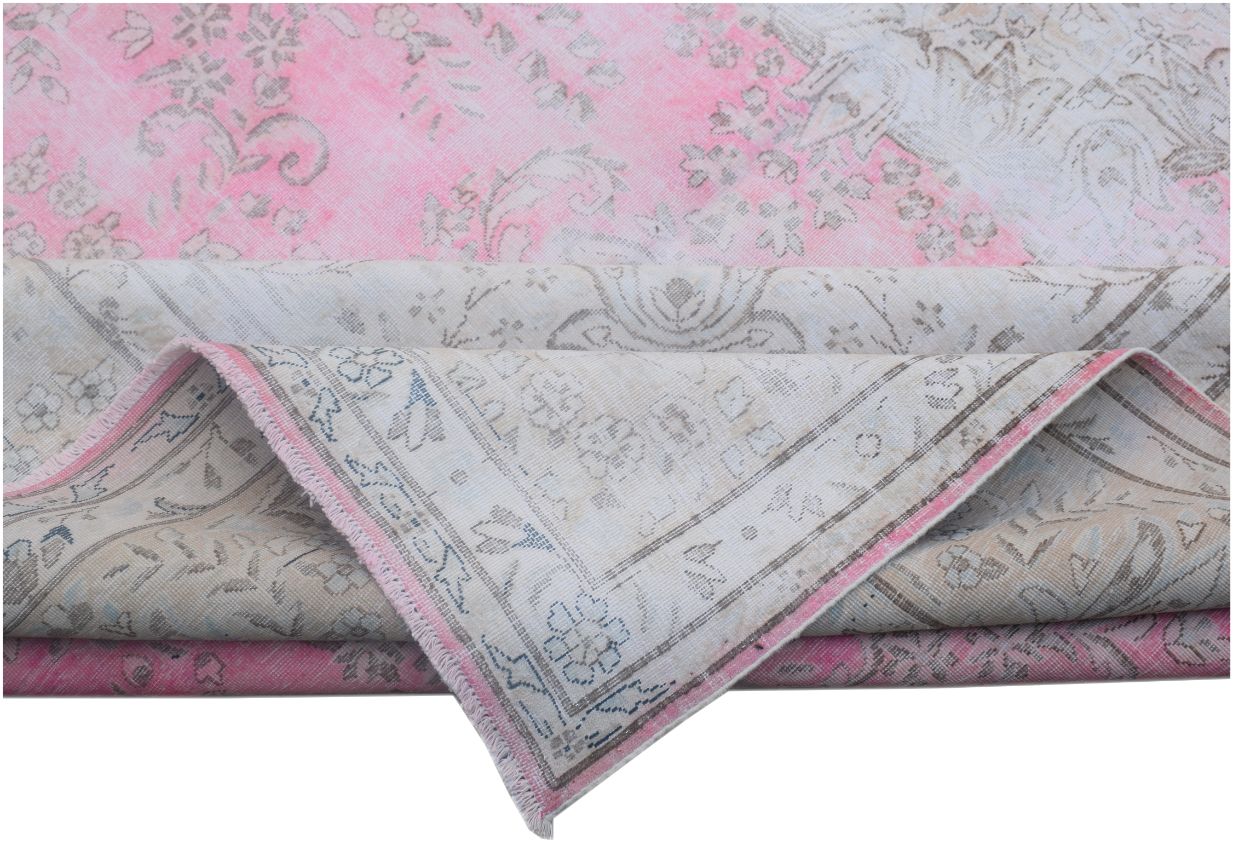 A vintage Persian Kerman rug featuring a faded pink and cream floral pattern with a folded corner.