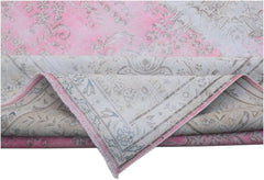A vintage Persian Kerman rug featuring a faded pink and cream floral pattern with a folded corner.