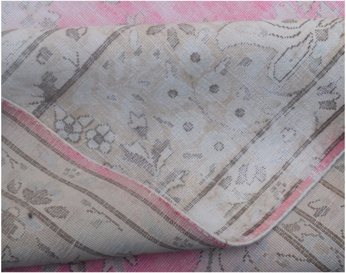 A vintage Persian Kerman rug featuring a faded floral pattern in soft pink and neutral tones.