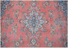 A vintage Persian Kerman rug featuring a central blue floral medallion on a coral field.