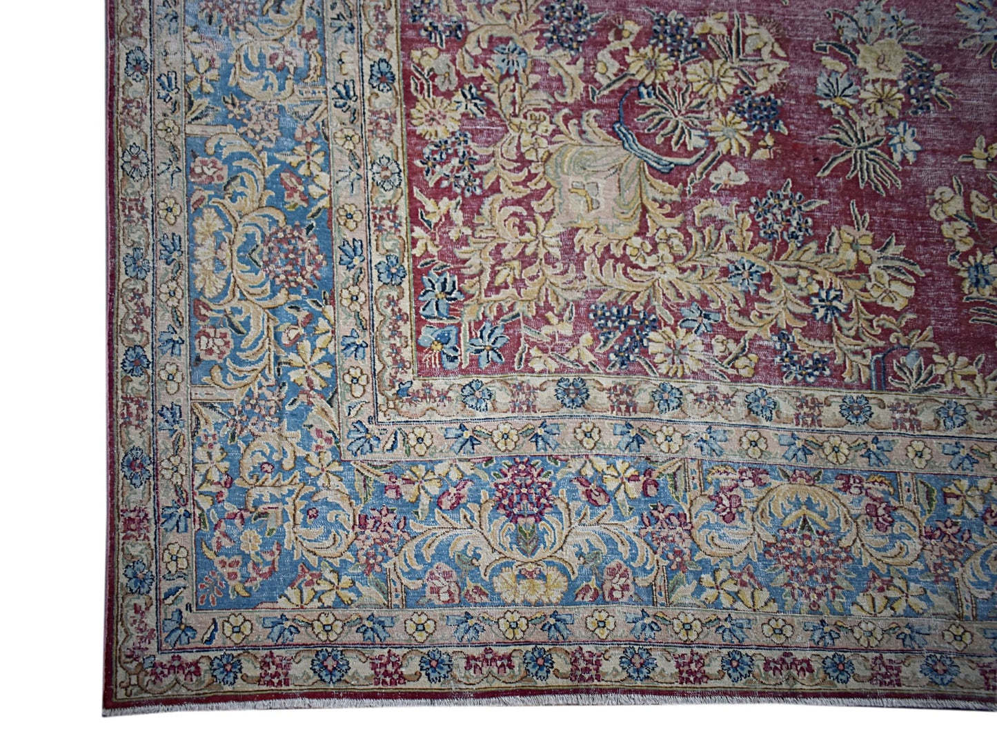 A vintage Persian Kerman rug featuring an intricate floral pattern in blue, red, and cream tones.