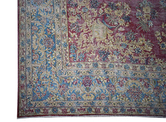 A vintage Persian Kerman rug featuring an intricate floral pattern in blue, red, and cream tones.