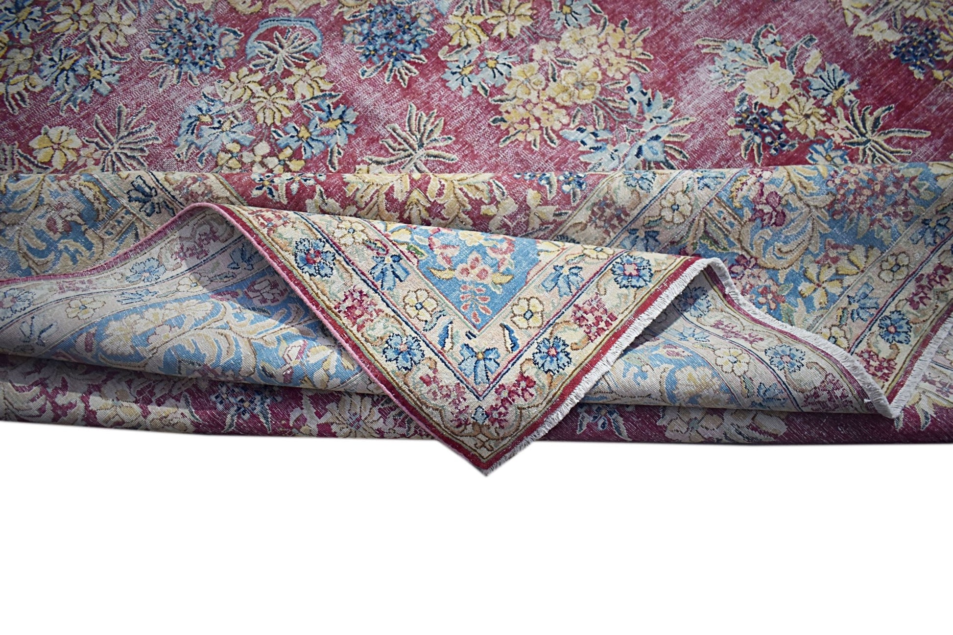 A vintage Persian Kerman rug featuring a deep red field with intricate floral patterns and a blue border.
