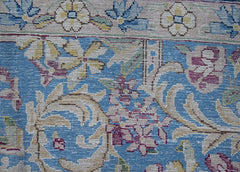 A close-up of a vintage Persian Kerman rug featuring intricate floral patterns on a blue field.