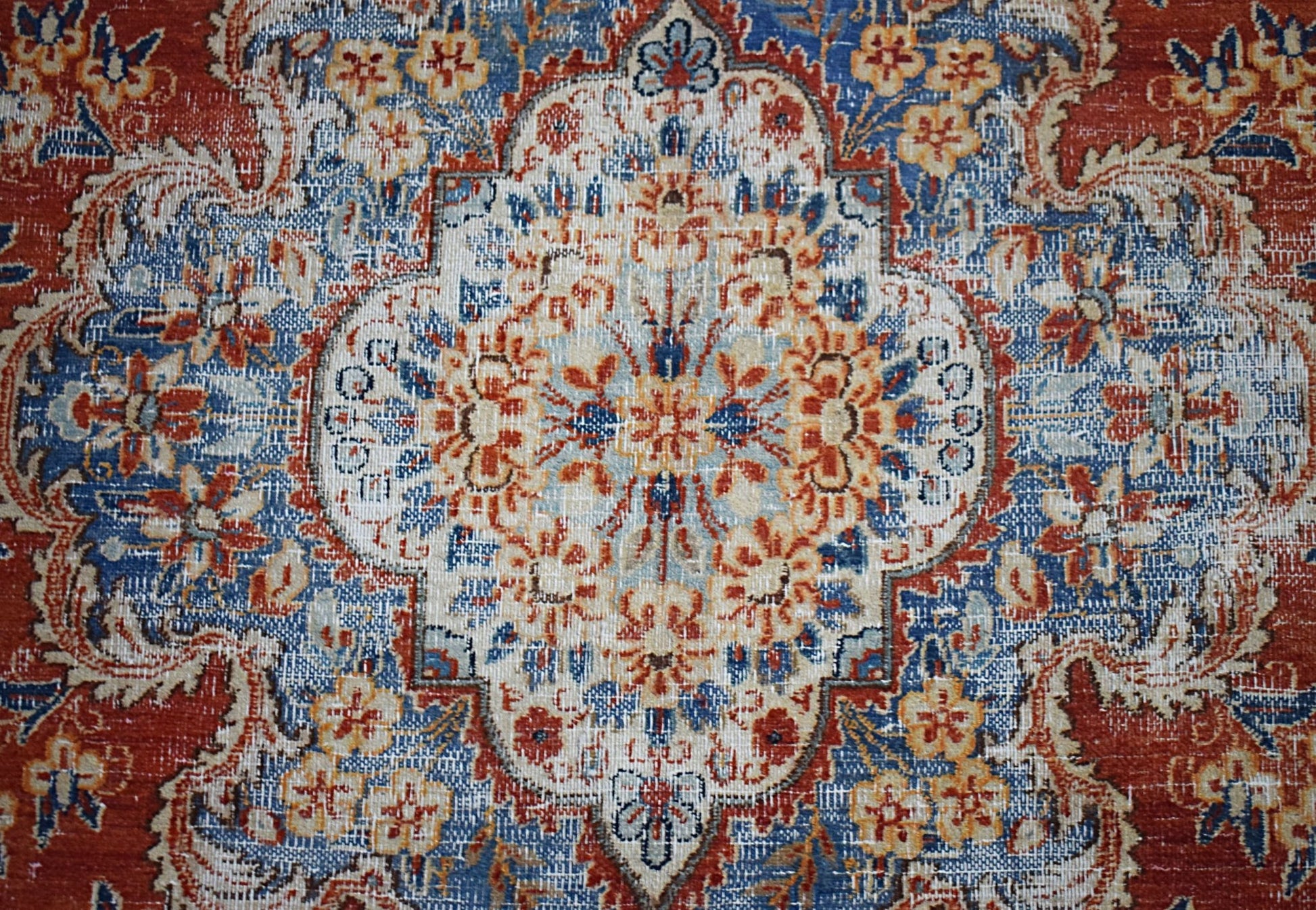 A vintage Persian Kerman rug featuring a central floral medallion in blue, red, and cream tones.