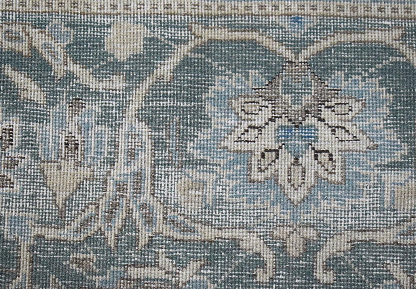 A close-up of a vintage Persian Kerman rug featuring intricate blue and beige floral patterns.