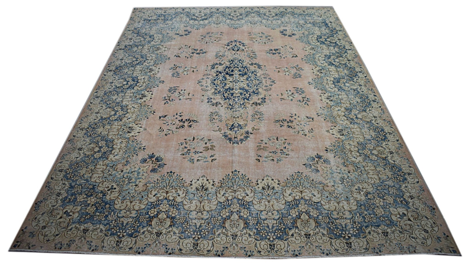 A vintage Persian Kerman rug featuring a central medallion and floral motifs in blue and peach.