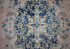 A vintage Persian Kerman rug featuring an intricate blue and cream floral medallion on a pink field.