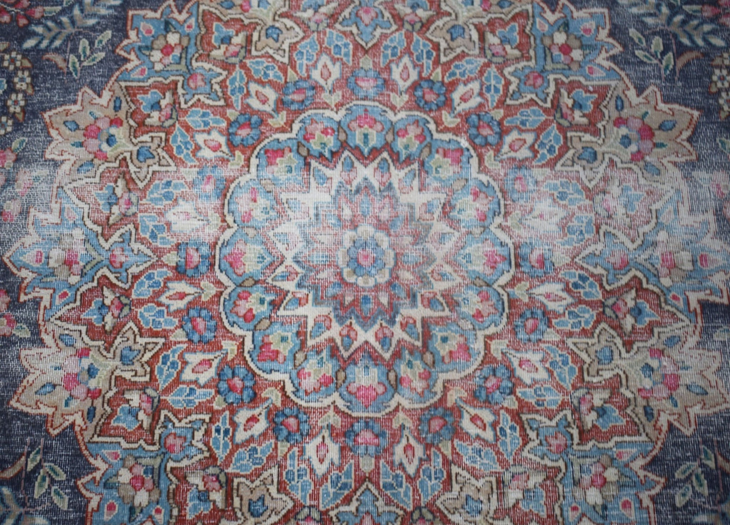 A vintage Persian Kerman rug featuring an intricate floral medallion in blue, red, and cream tones.