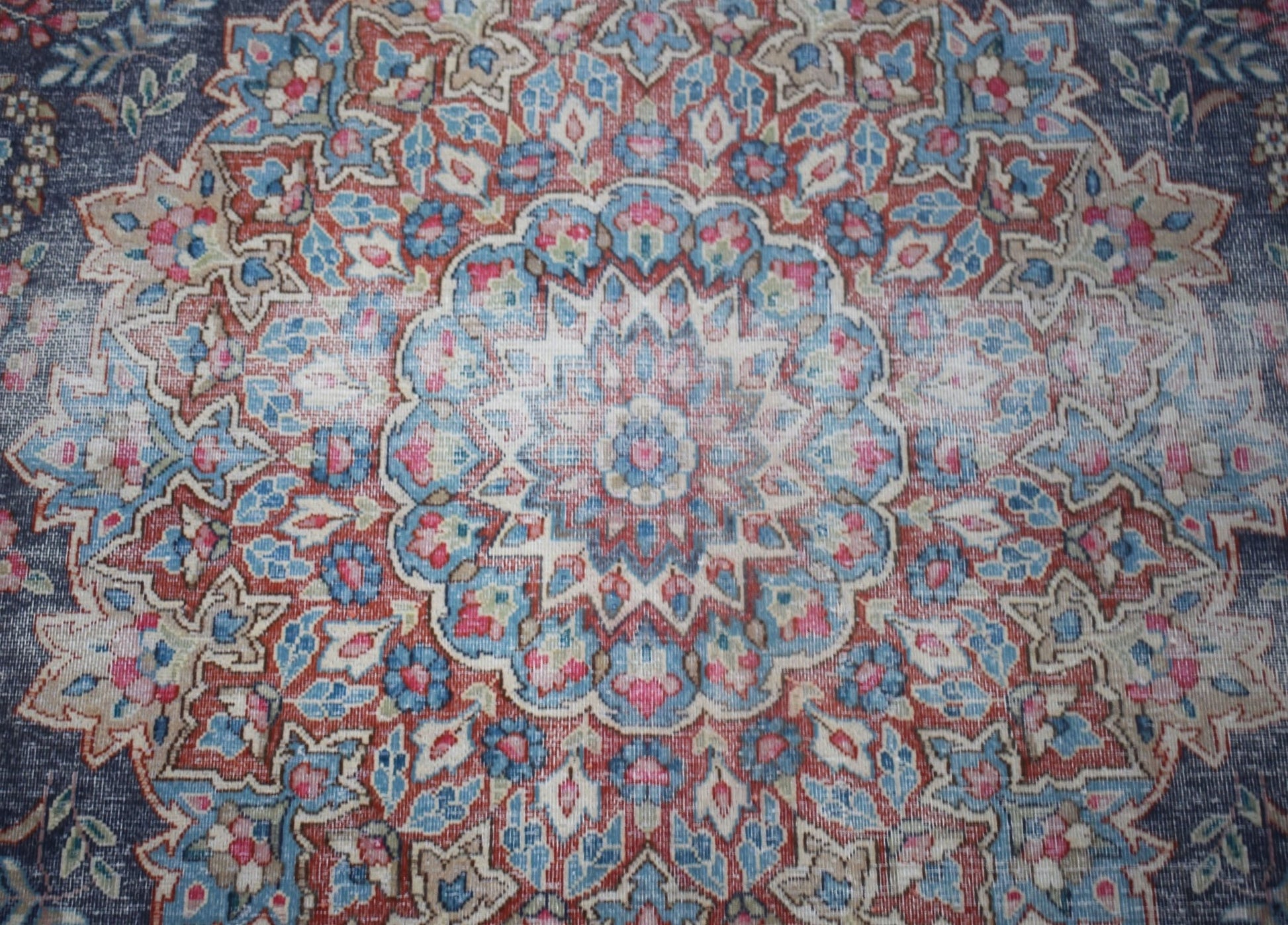 A vintage Persian Kerman rug featuring an intricate floral medallion in blue, red, and cream tones.