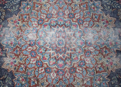 A vintage Persian Kerman rug featuring an intricate floral medallion in blue, red, and cream tones.