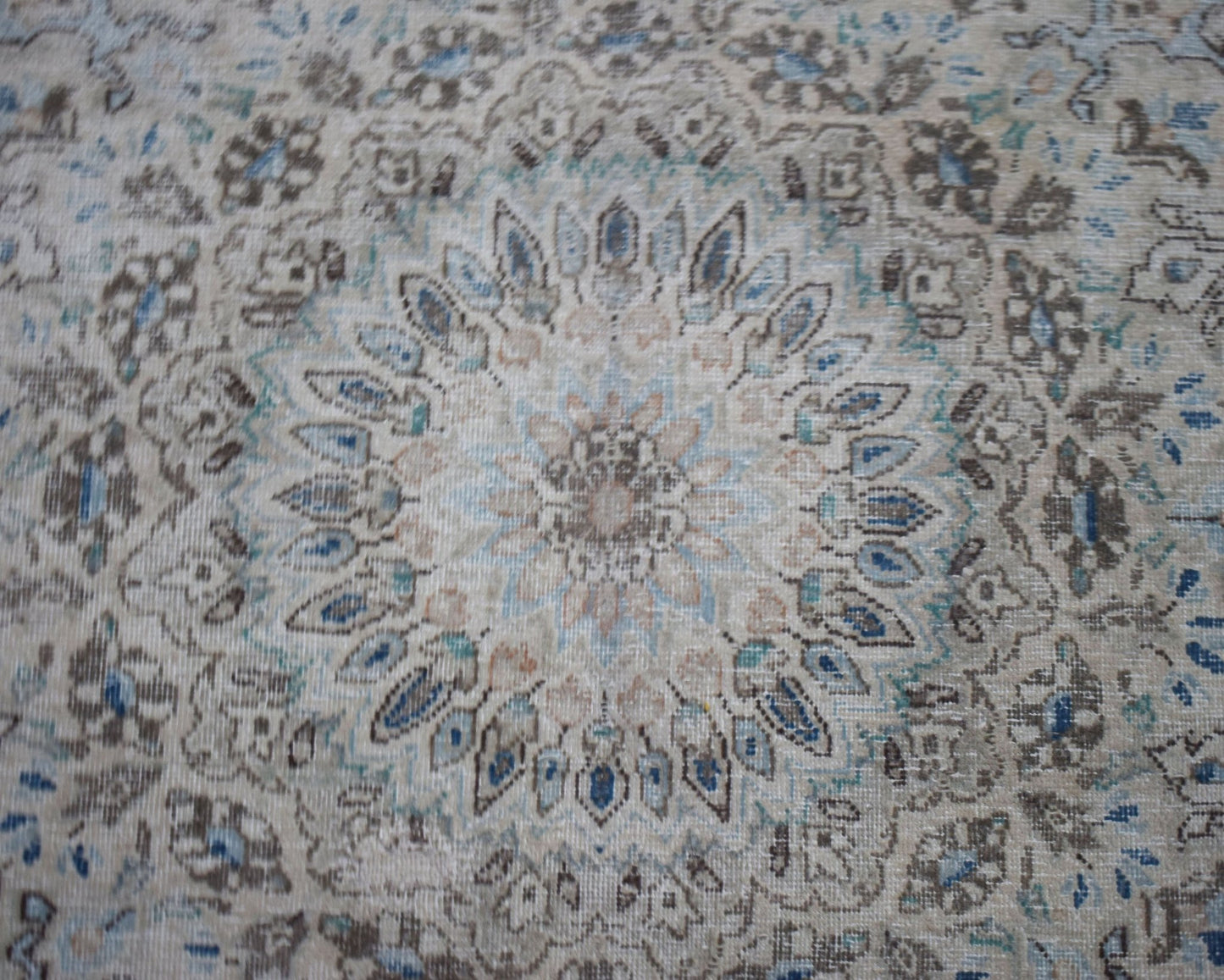 A vintage Persian Kerman rug featuring an intricate floral medallion in soft blue and beige tones.