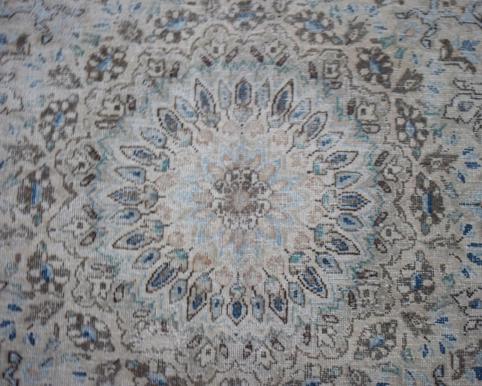 A vintage Persian Kerman rug featuring an intricate floral medallion in soft blue and beige tones.