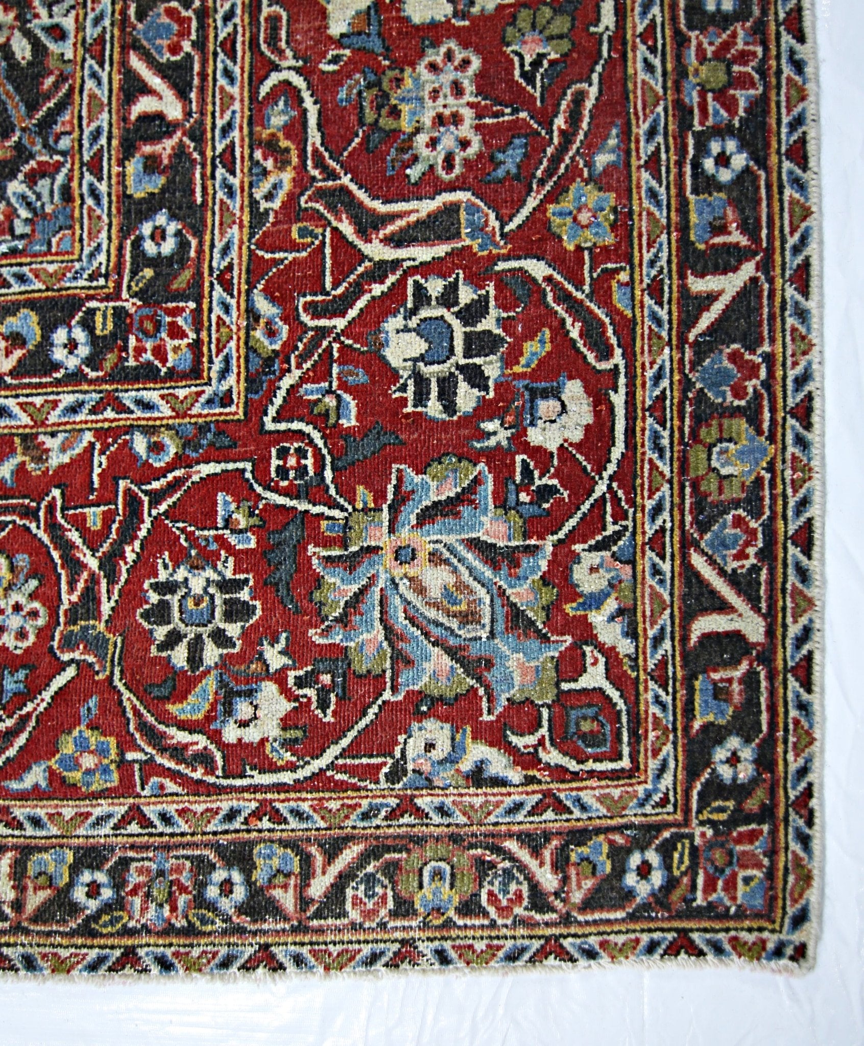 A vintage Persian Kerman rug featuring an intricate floral pattern in red, blue, and cream tones.