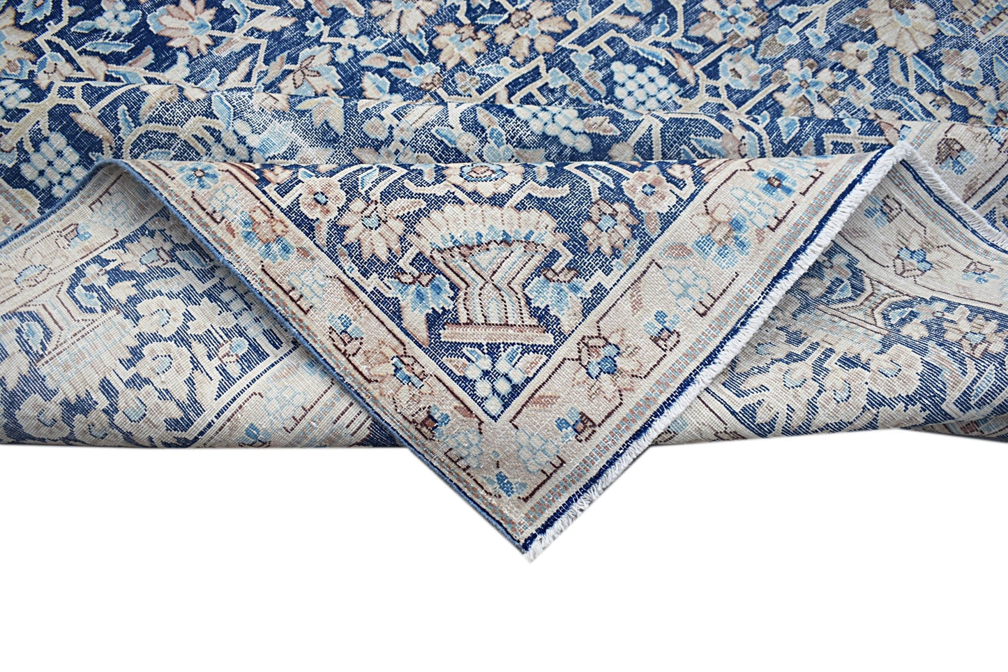 A vintage Persian Kerman rug featuring a blue and beige floral pattern with a folded corner.