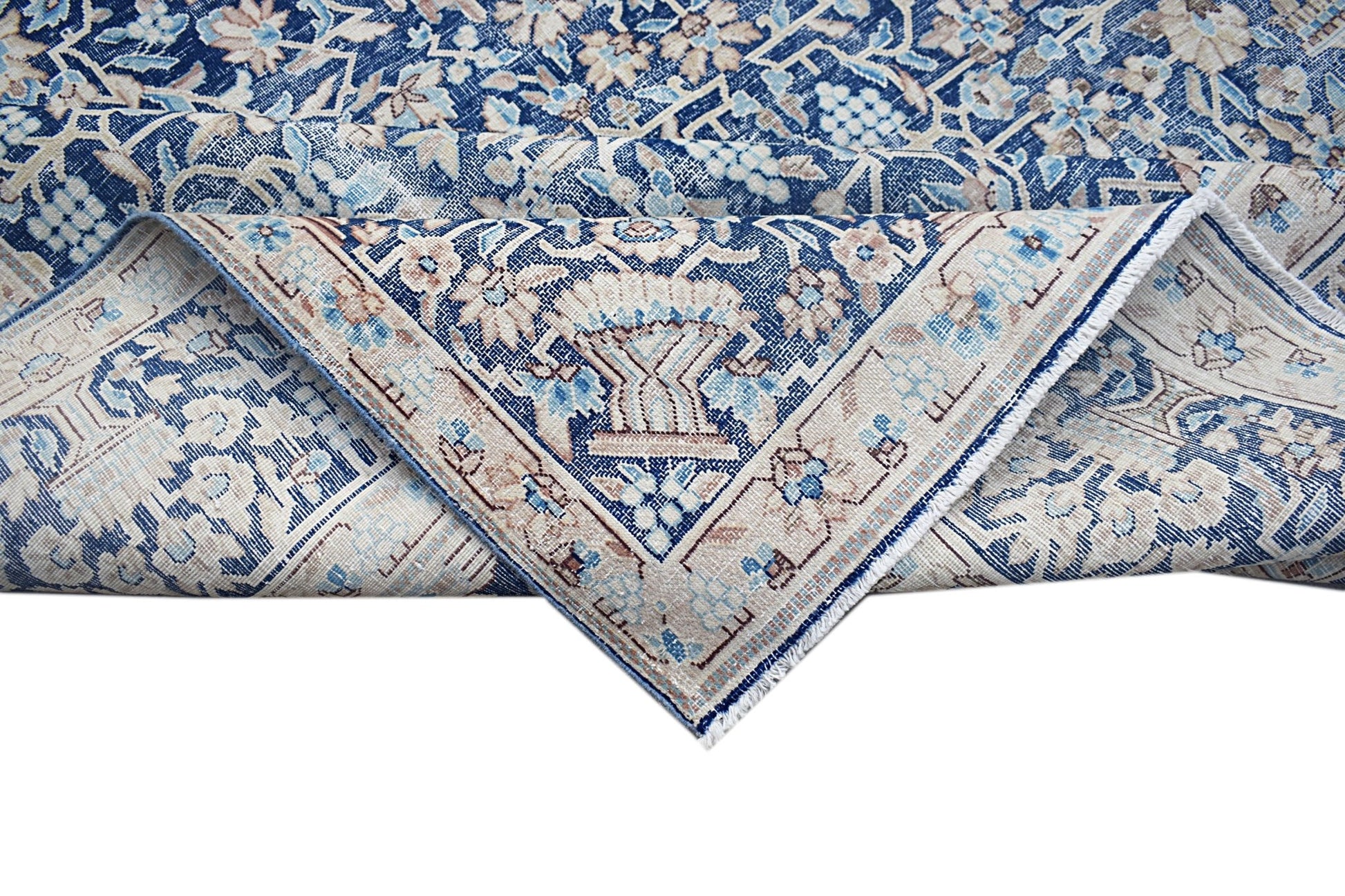 A vintage Persian Kerman rug featuring a blue and beige floral pattern with a folded corner.