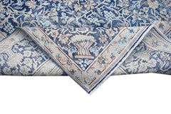 A vintage Persian Kerman rug featuring a blue and beige floral pattern with a folded corner.