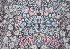 Vintage Persian Kerman rug with a floral pattern in pink, blue, and white on a dark background.