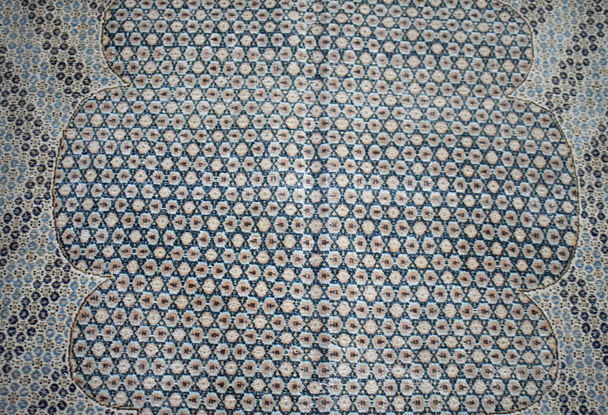 A vintage Persian Kerman rug featuring an intricate, repeating geometric pattern in blue and beige.