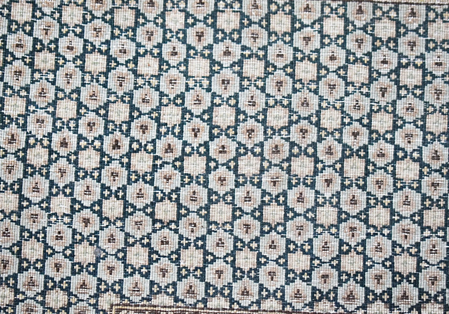 A vintage Persian Kerman rug featuring a repeating geometric pattern in muted tones.