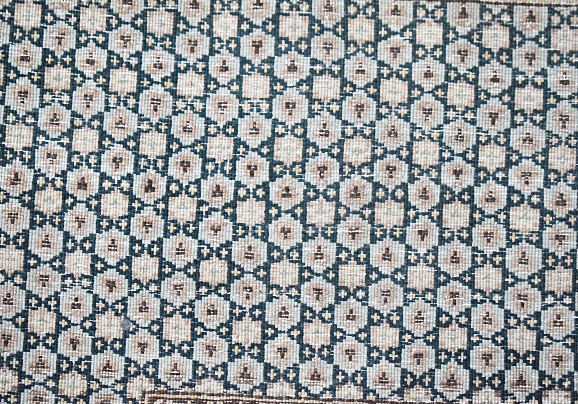 A vintage Persian Kerman rug featuring a repeating geometric pattern in muted tones.