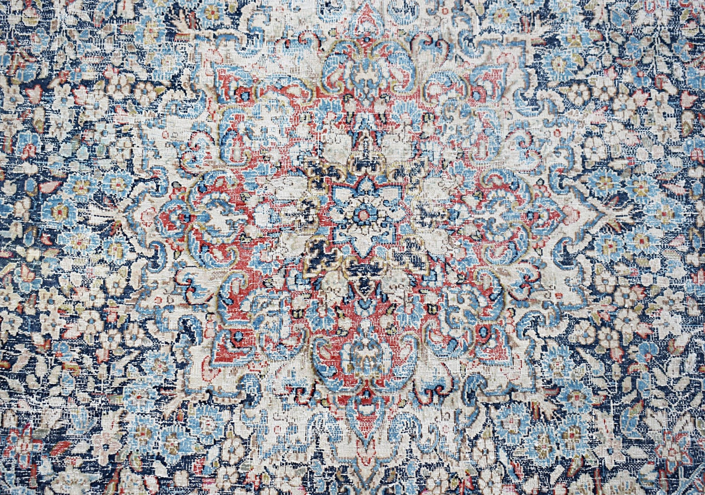 A vintage Persian Kerman rug featuring an intricate floral medallion in blue, red, and cream tones.
