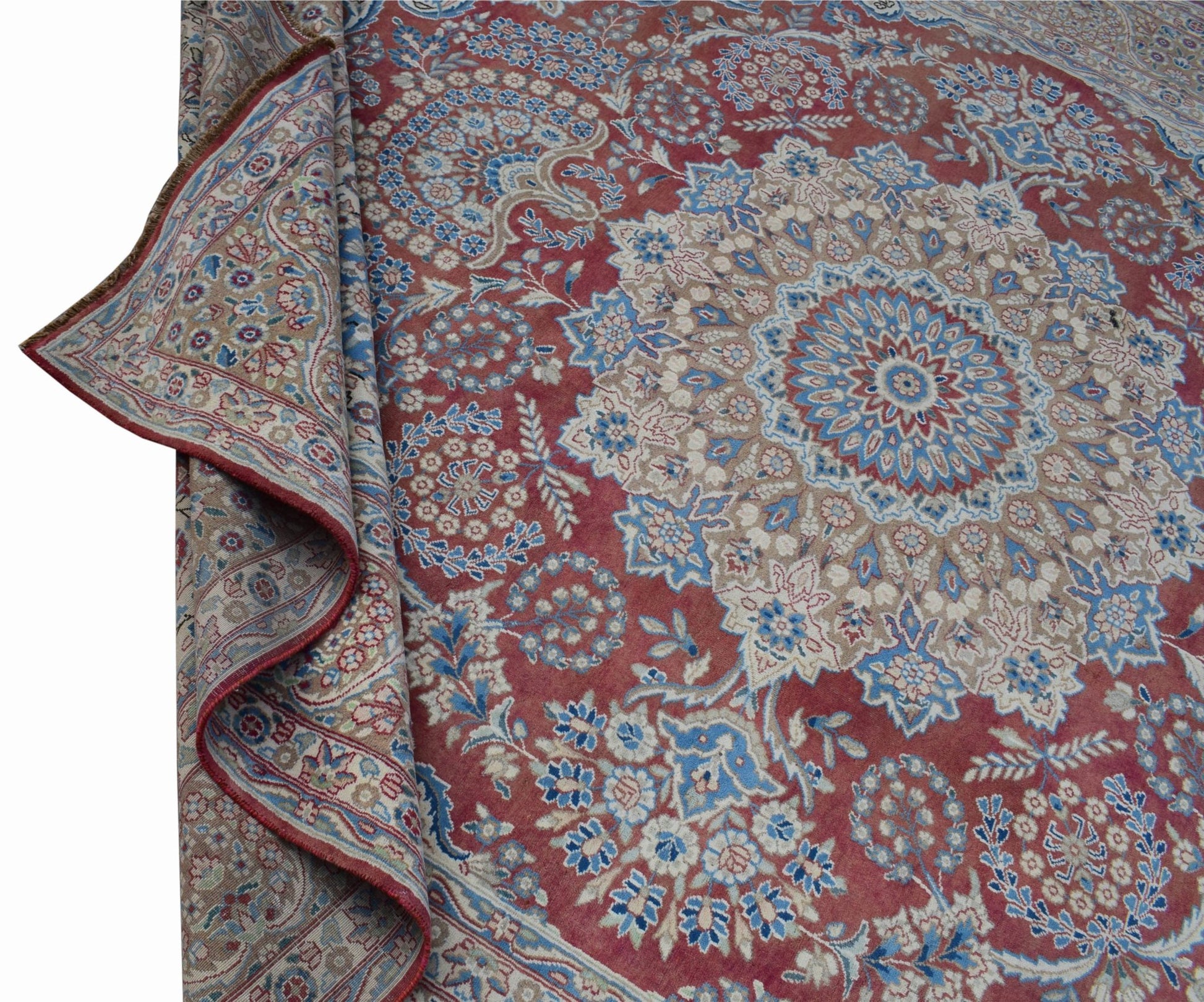 A vintage Persian Kerman rug featuring a central floral medallion on a red field with blue accents.