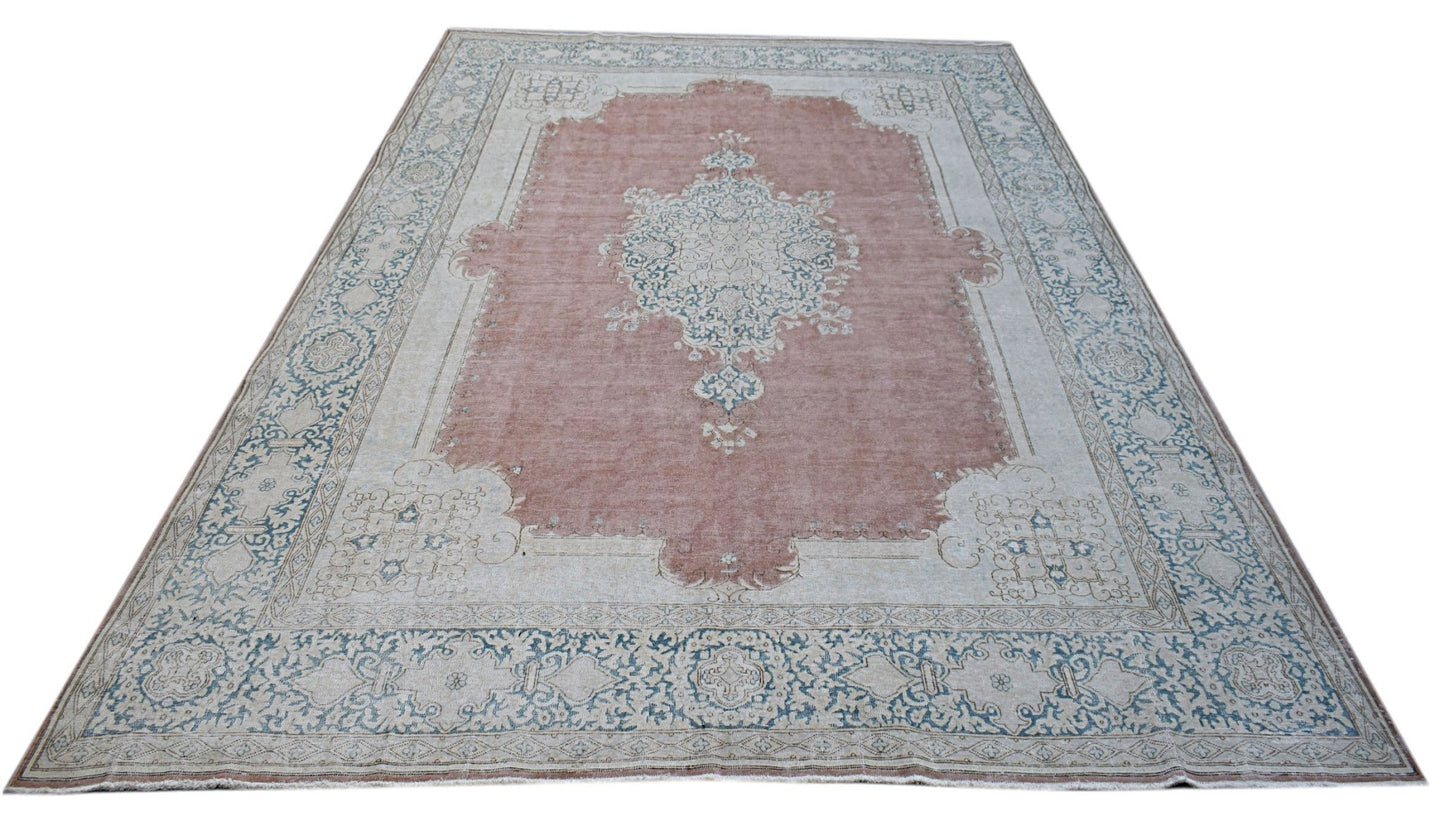A vintage Persian Kerman rug featuring a central medallion on a dusty pink field with blue floral borders.