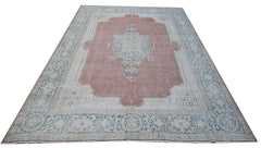 A vintage Persian Kerman rug featuring a central medallion on a dusty pink field with blue floral borders.