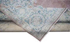 A vintage Persian Kerman rug featuring a blue floral medallion pattern on a soft pink background.