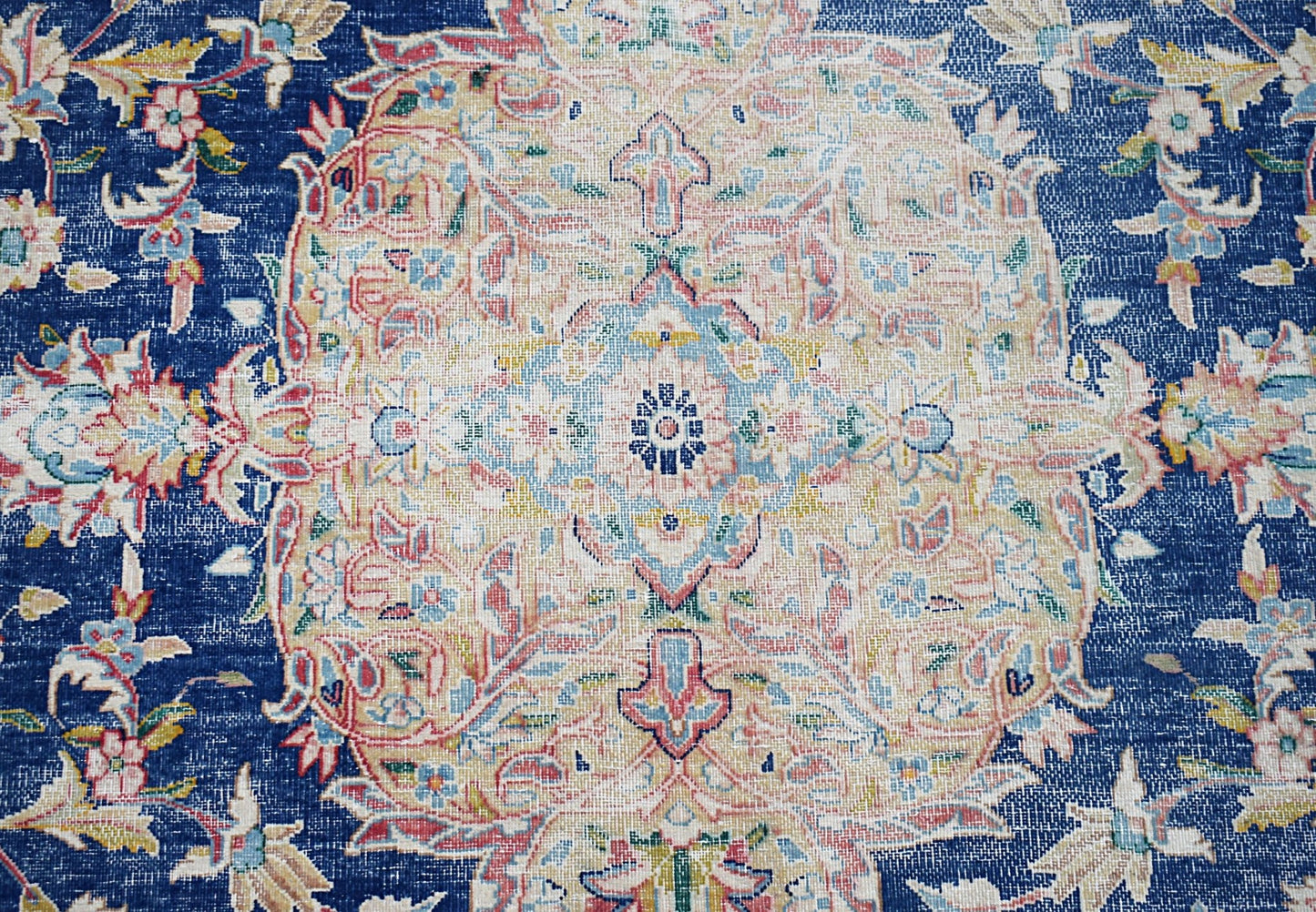A vintage Persian Kerman rug featuring an intricate floral medallion on a deep blue background.
