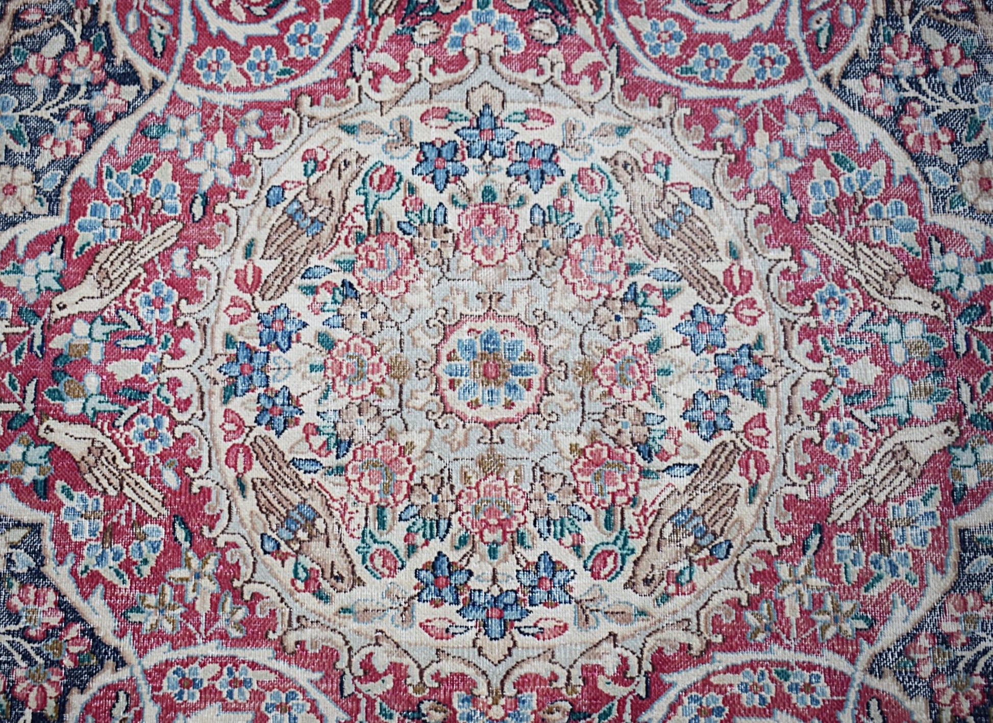 A vintage Persian Kerman rug featuring an intricate floral medallion design in red and blue tones.