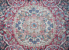 A vintage Persian Kerman rug featuring an intricate floral medallion design in red and blue tones.