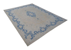 A vintage Persian Kerman rug featuring a central medallion and blue floral motifs on a beige field.