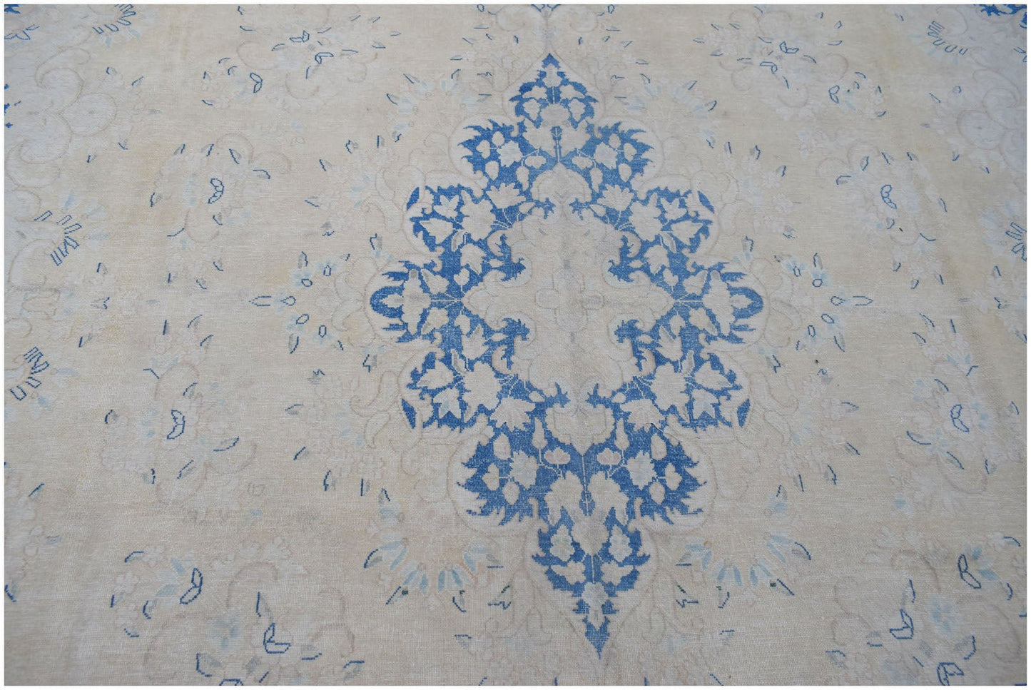 A vintage Persian Kerman rug featuring a central blue floral medallion on a cream background.