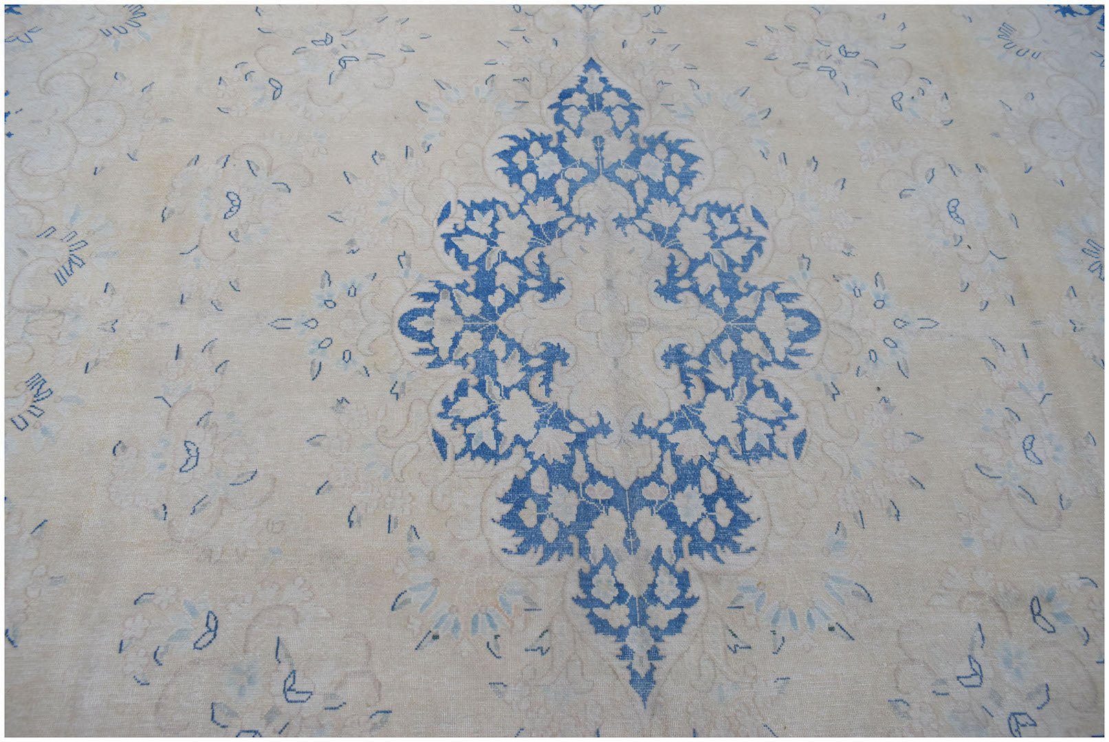 A vintage Persian Kerman rug featuring a central blue floral medallion on a cream background.