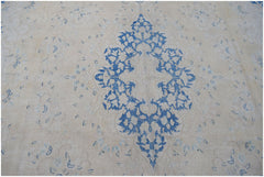 A vintage Persian Kerman rug featuring a central blue floral medallion on a cream background.