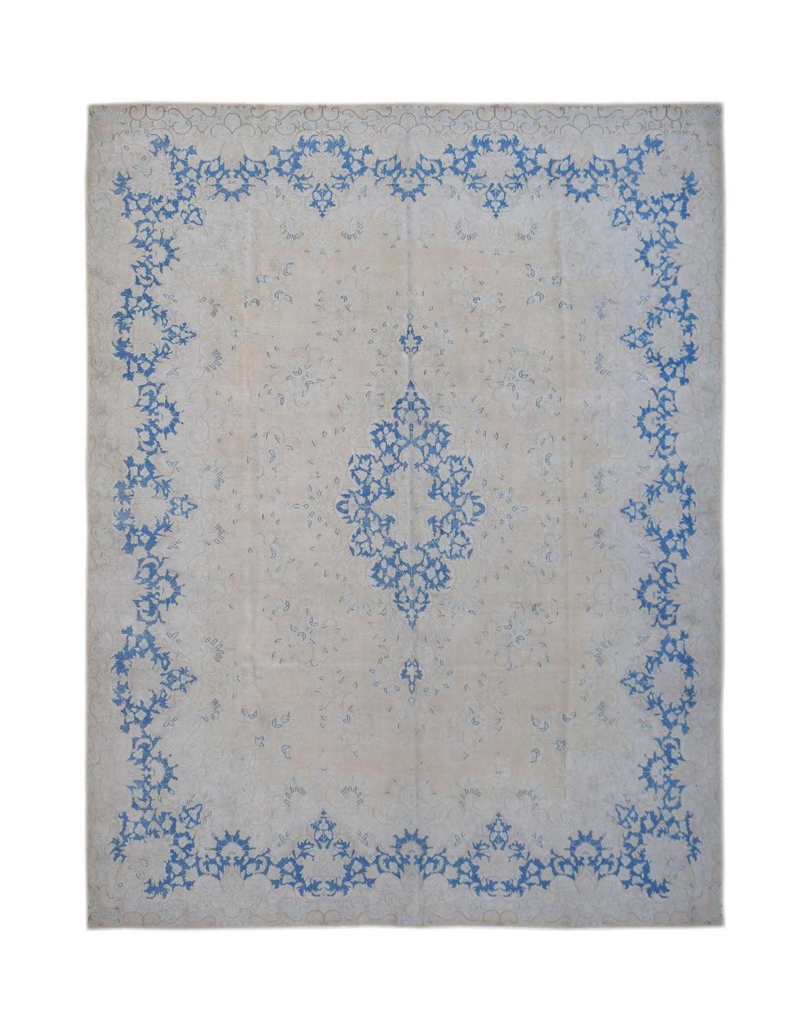 A vintage Persian Kerman rug featuring a blue floral medallion and border on a beige background.