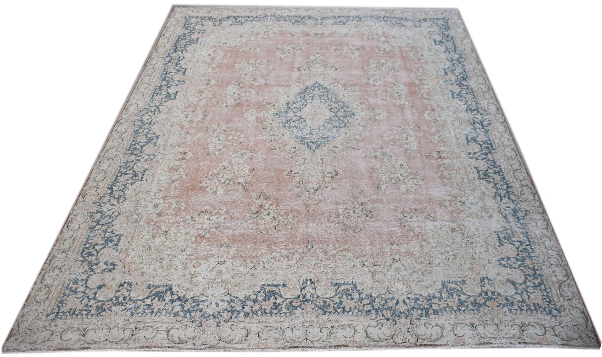 A vintage Persian Kerman rug featuring a central medallion and floral motifs in soft pink and blue.