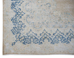 A vintage Persian Kerman rug featuring a blue floral medallion pattern on a beige background.