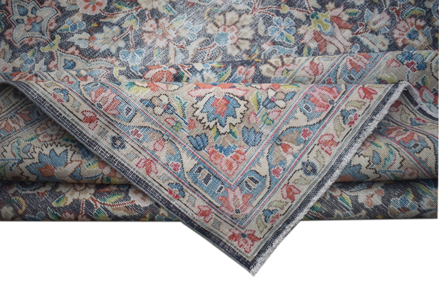 A vintage Persian Kerman rug featuring an intricate floral pattern and a folded corner.