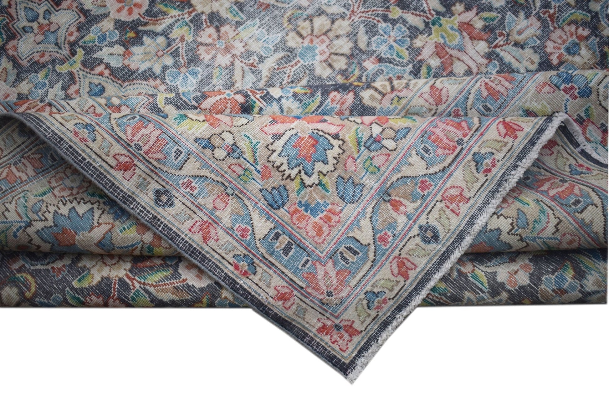 A vintage Persian Kerman rug featuring an intricate floral pattern and a folded corner.