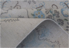 A close-up of a vintage Persian Kerman rug featuring a floral pattern in blue and grey tones.