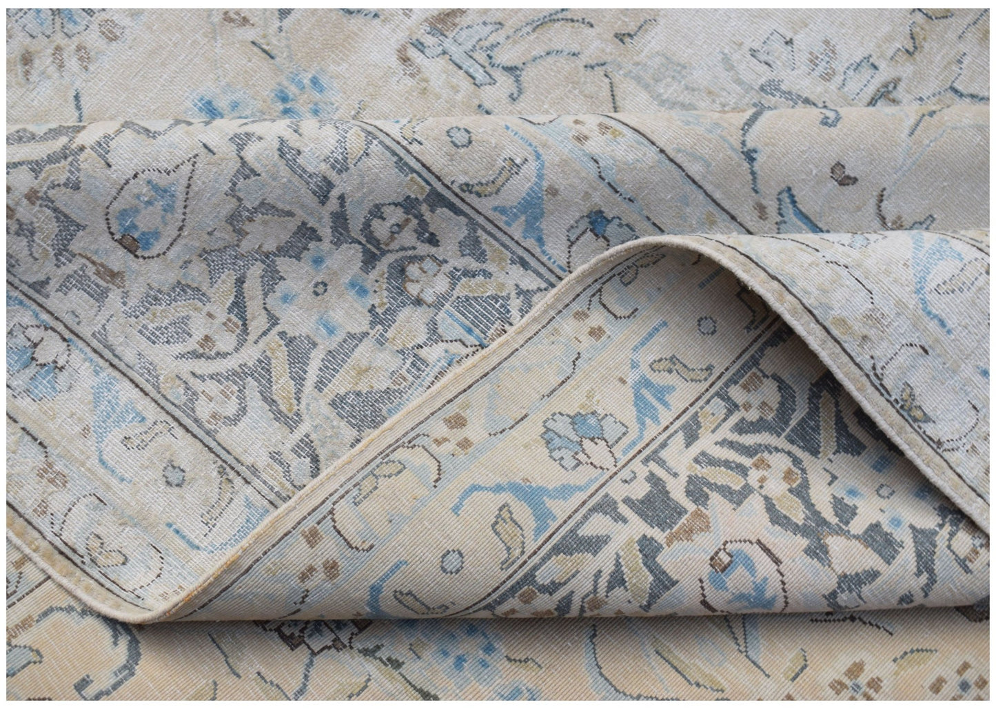 A vintage Persian Kerman rug with a folded corner revealing intricate floral and medallion patterns.