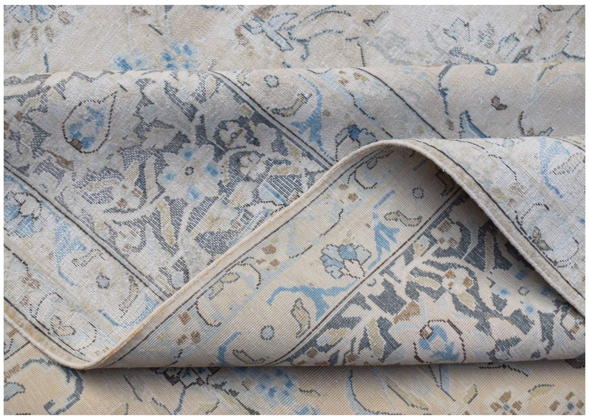 A vintage Persian Kerman rug with a folded corner revealing intricate floral and medallion patterns.